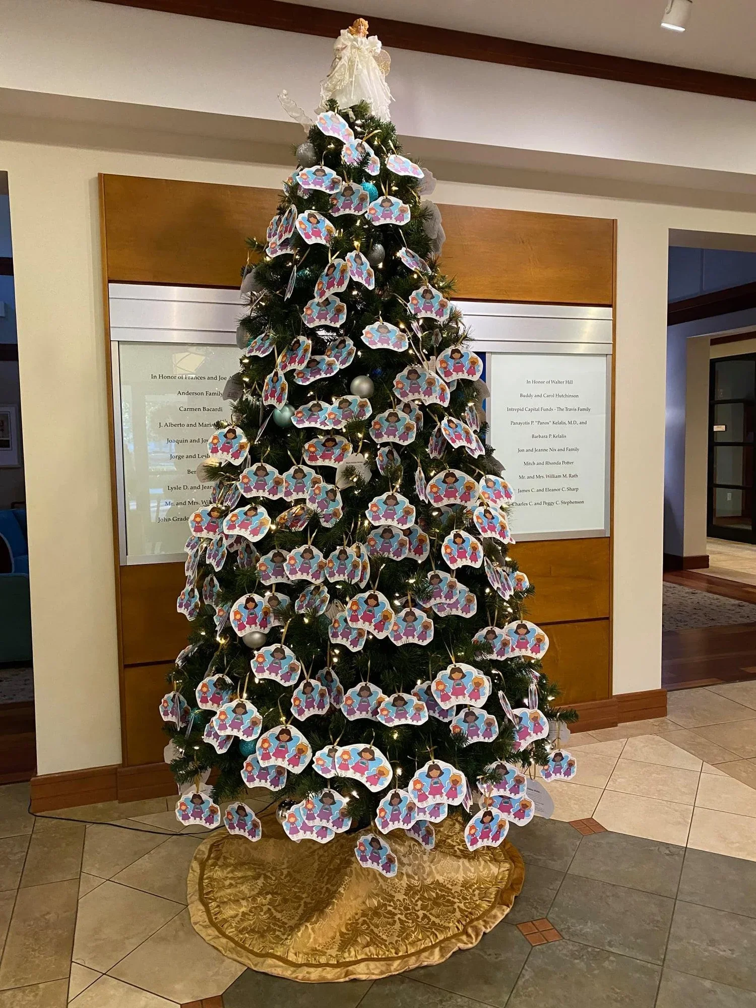 Decorated Christmas tree with paper angels and ornaments, on a gold tree skirt in an indoor setting.