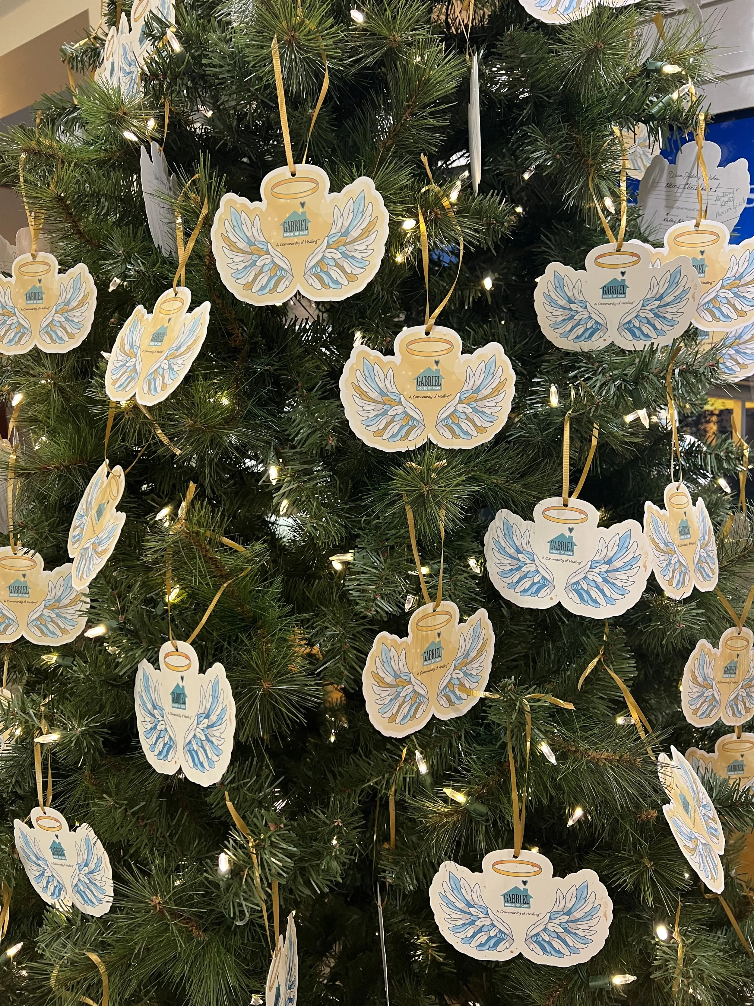 A decorated Christmas tree adorned with angel wing and halo ornaments featuring the Gabriel House of Care logo.