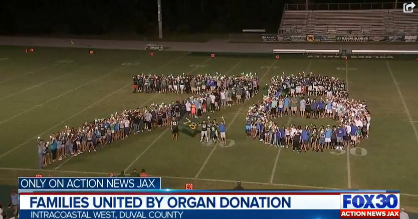 Large group of people forming the words 'THANK YOU' on a football field at night