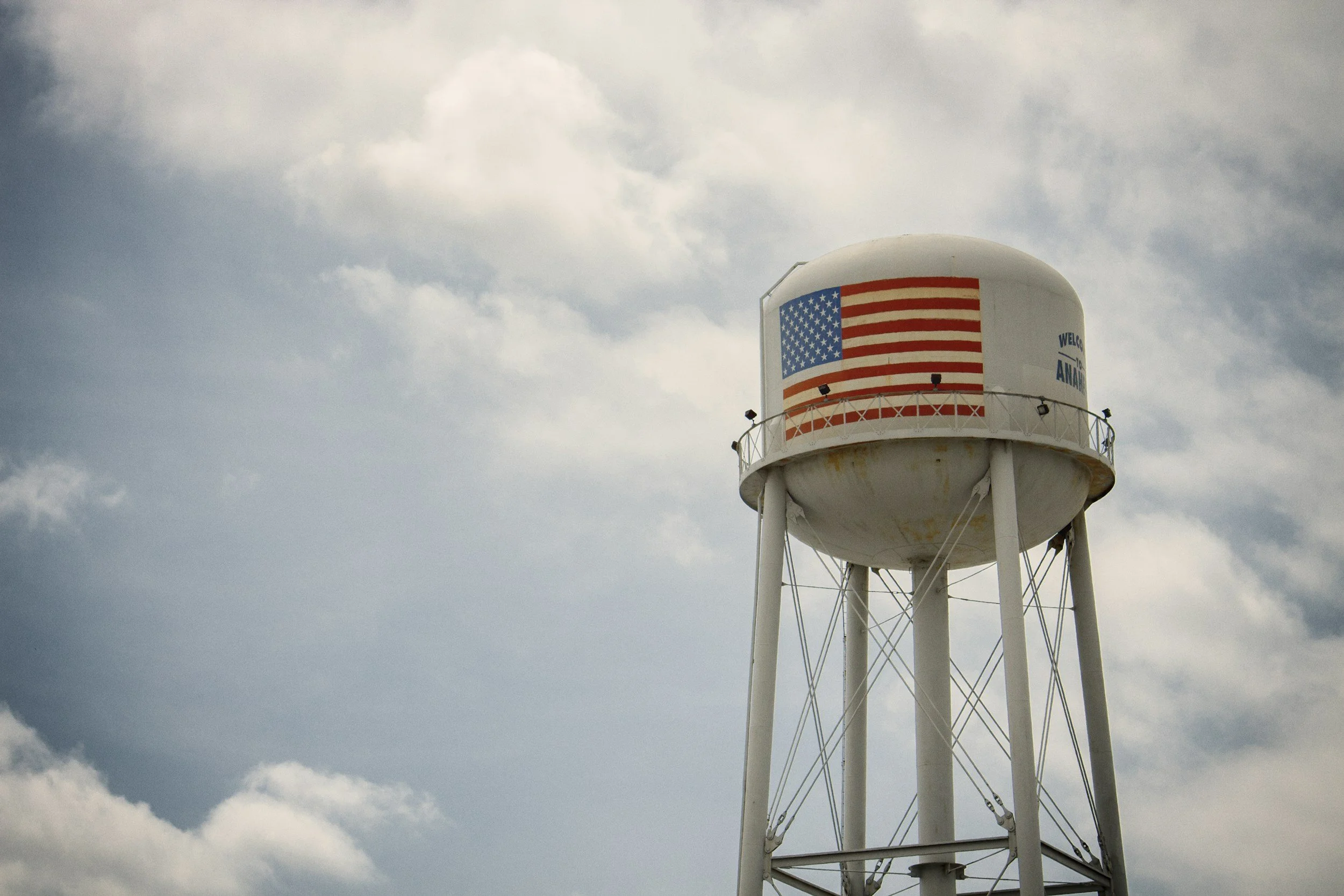 A water tower with an American flag design painted on it, set against a cloudy sky.
