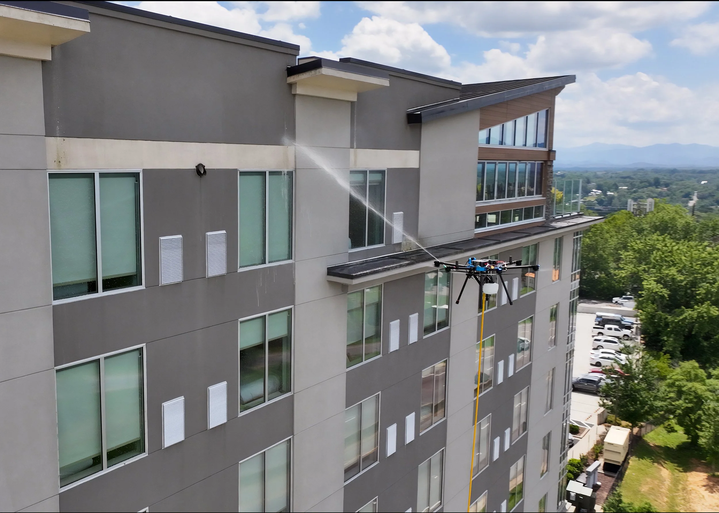 A drone flying near a high-rise building with a water spray device attached, spraying water on the building's exterior during daytime.