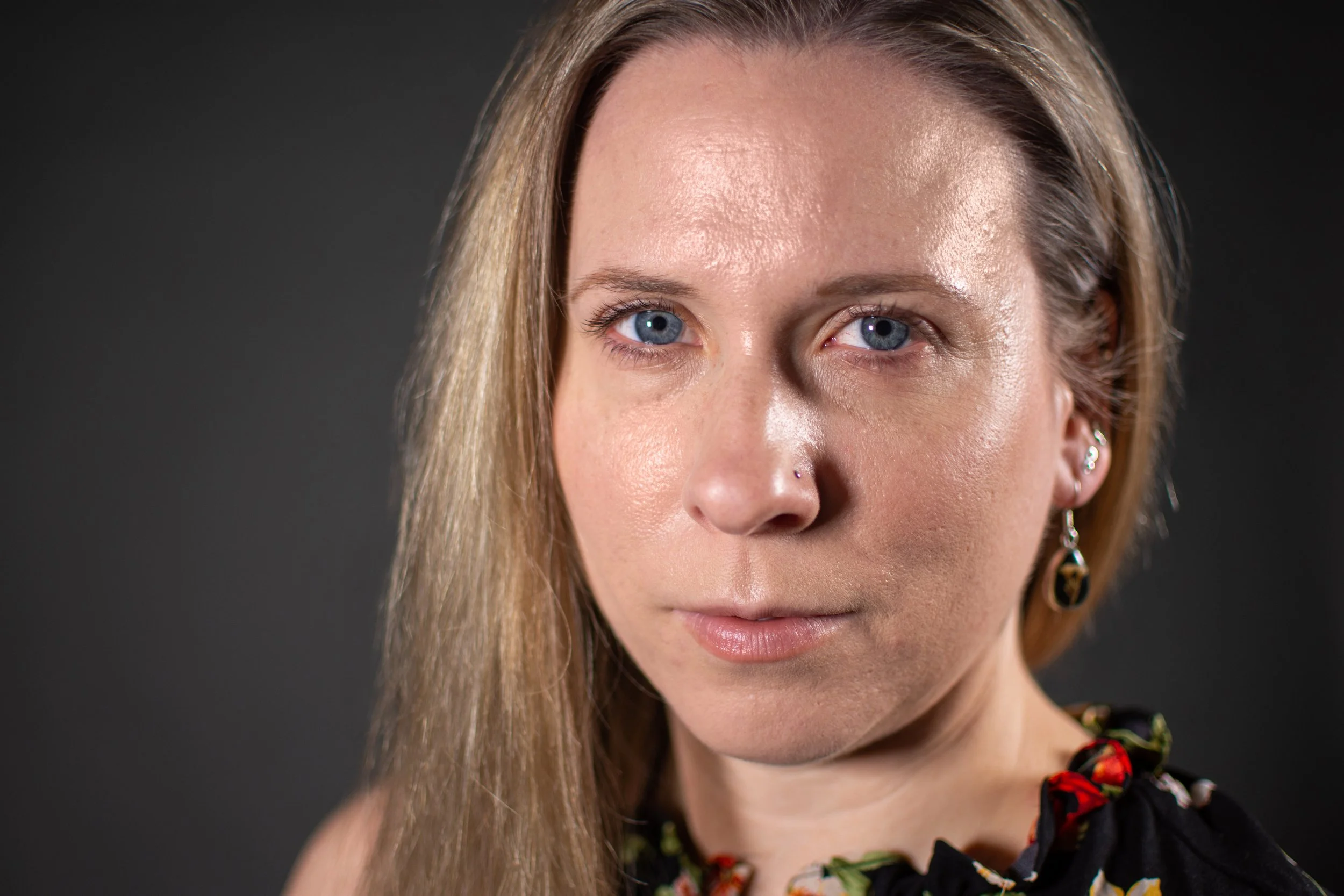 Close-up of a woman with blonde hair, blue eyes, and earrings, wearing a floral patterned top.