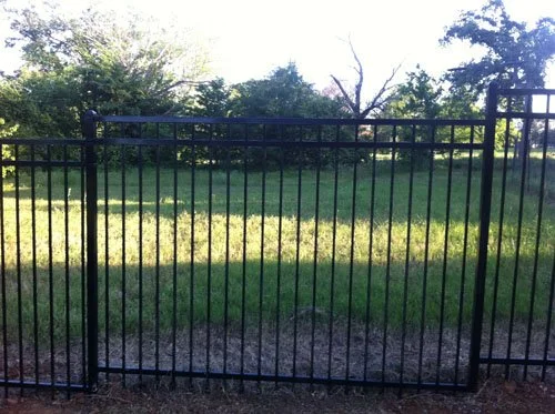 A black metal gate with vertical bars, situated in front of a grassy area with trees in the background.