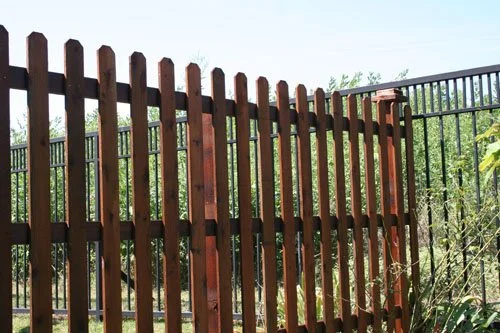 Wooden fence with vertical slats and a metal gate in an outdoor setting with greenery.