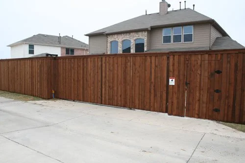 A tall wooden privacy fence blocking the view of the house behind it, with a small gate on the right side.