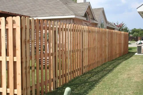 New wooden privacy fence along a backyard, with neighboring houses visible in the background.