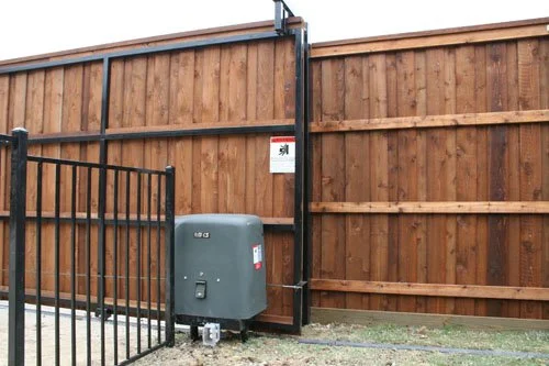 A wooden privacy fence with a small metal gate, an electric meter box, and a warning sign.