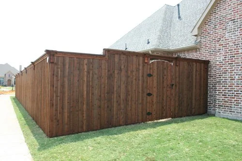 Privacy fence made of wood next to brick house with grassy yard.
