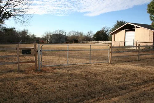 Fenced rural property with a barn and open field in the background.