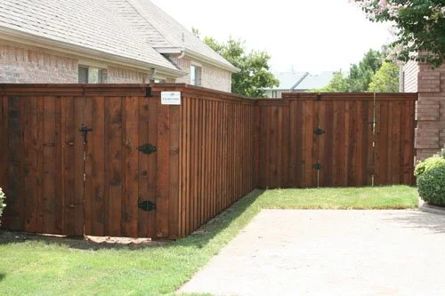 Wooden privacy fence with a gate, next to a gravel driveway and grassy lawn.