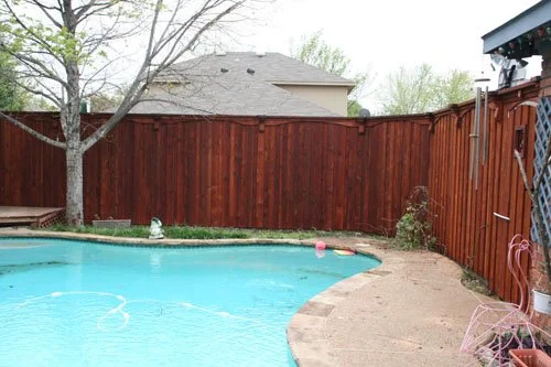 Backyard with a swimming pool, a wooden fence, a tree, and some outdoor furniture.