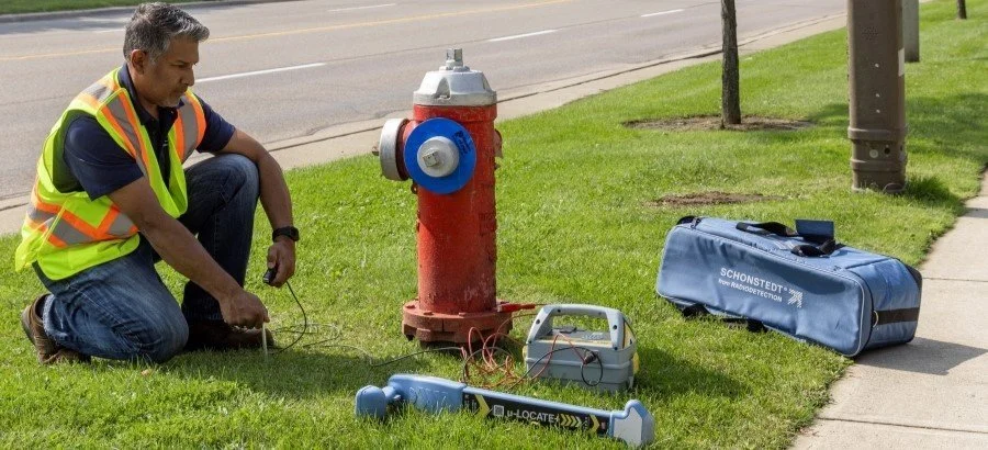 Technician kneeling beside a fire hydrant setting up a Schonstedt u-LOCATE locator and equipment case.
