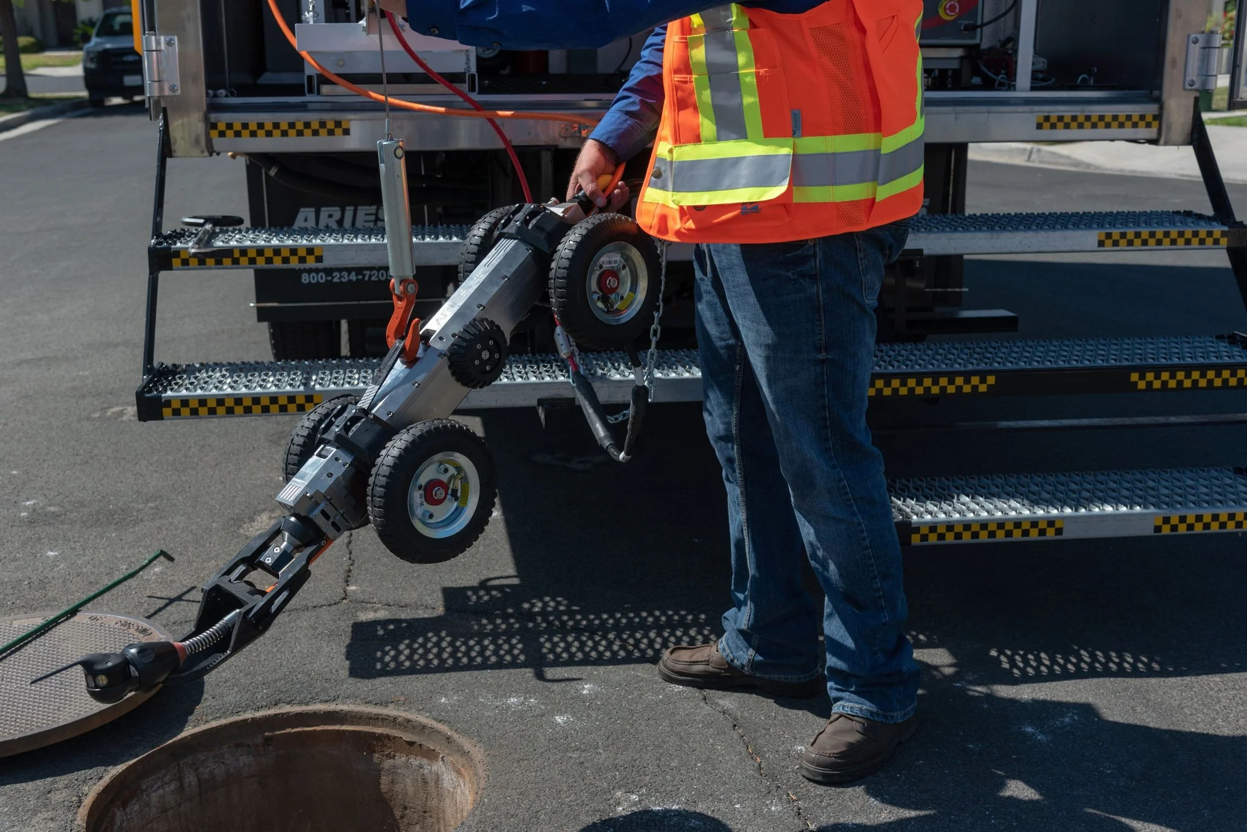 Technician in safety vest handling the LETS 6.0 crawler at a manhole during a sewer inspection.