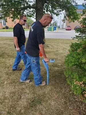 Two technicians using a Schonstedt locator on a grassy area during outdoor training or fieldwork.