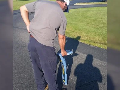 Technician bending down to use a locator wand along a paved edge.