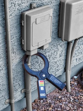 Rycom Clampmitter signal clamp attached to underground utility conduit near an electrical junction box.