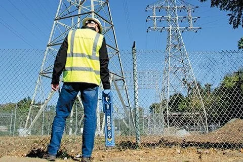 Technician in a high-visibility vest operating a Radiodetection locator near high-voltage transmission towers.