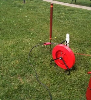 Red utility marking wheel and cable reel set up on grass.