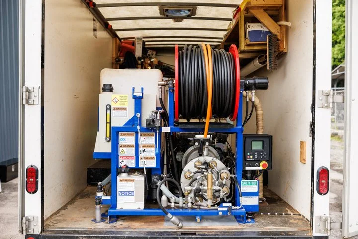 Truck-mounted hydro jetting unit with hose reel, tank, and control panel installed in the vehicle's cargo area.