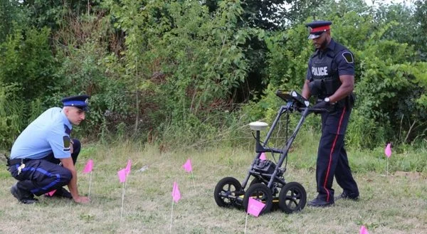 Police officers using a Radiodetection LMX GPR cart alongside marker flags during a forensic ground search.