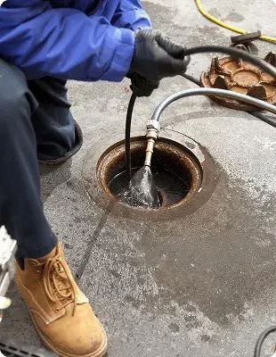 Hydro jetting nozzle spraying water into a manhole opening during sewer line cleaning.