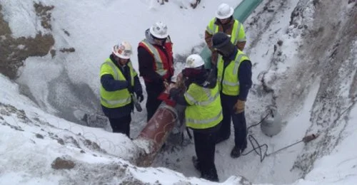 Crew in hard hats and safety vests working in a snow-covered excavation trench.