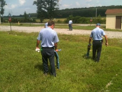 Two technicians locating utilities in an open grass field with hills in the background.