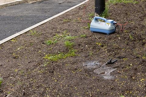 Radiodetection Earth Mat connected to a transmitter on gravel near a paved road edge.