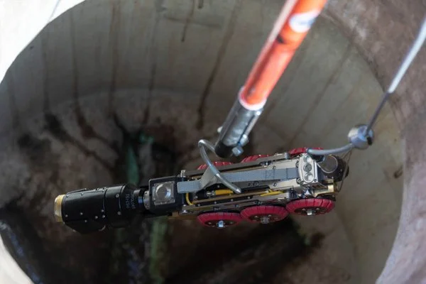 Pipe inspection crawler camera with wheeled tractor unit being lowered into a large diameter culvert for CCTV inspection.