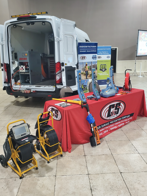 Locator Guys trade show booth featuring a service van, pipe inspection camera reels, and product display table.