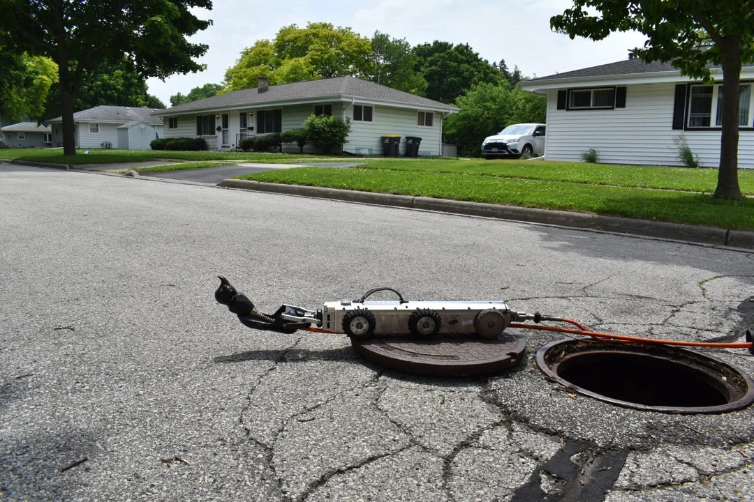Aries mainline sewer crawler positioned at a manhole opening on a residential street before deployment.
