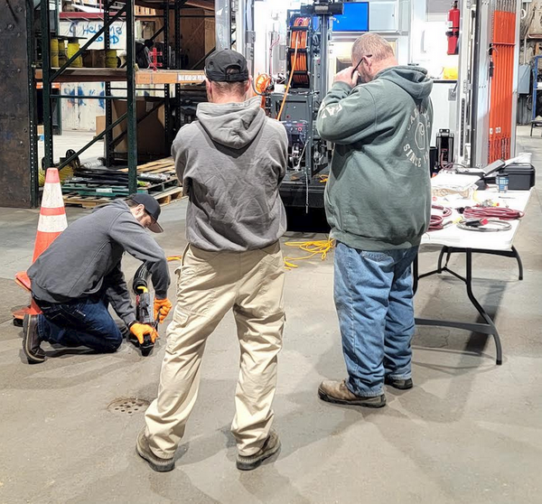 Group of technicians gathered around a manhole during sewer inspection equipment training in a warehouse facility.