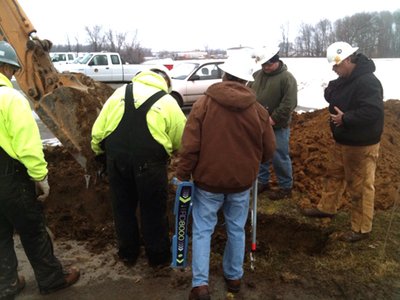 Crew excavating a muddy pit in snowy field conditions.