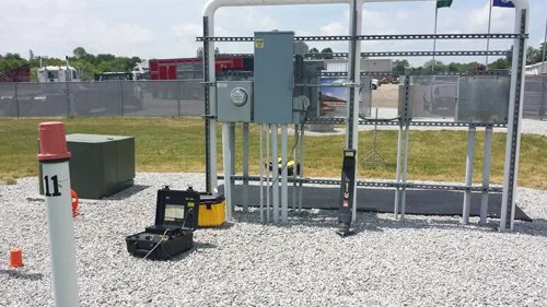 Locating equipment set on gravel near a fenced utility control station.