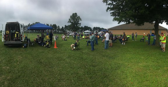 Wide view of a large group gathered outdoors under a canopy tent for a training event.