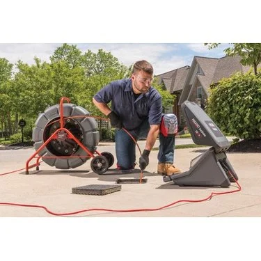 Technician operating a RIDGID SeeSnake camera reel and monitor during a residential pipe inspection job.