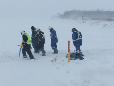 Crew locating utilities across a snow-covered field, marking flags placed in the snow.