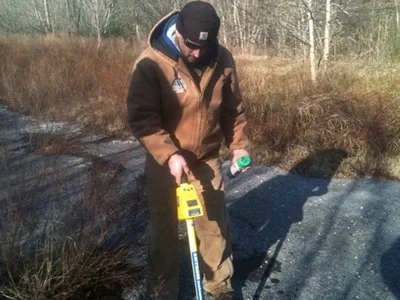 Technician using a locating device near a rocky embankment.