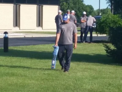 Technician walking across grass carrying a locator wand near a building.