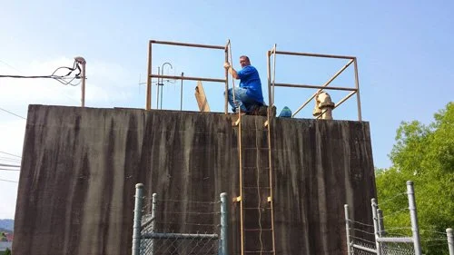 Worker standing on an elevated wooden structure with a metal support frame.