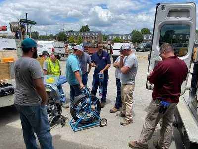 Group of technicians gathered around a portable pipeline inspection reel system during outdoor field equipment training.