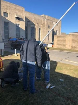 Group of technicians standing near a building looking toward an overhead line or pole.