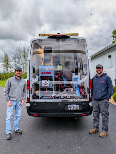 Two Locator Guys technicians standing beside a service van outfitted with a mainline pipeline inspection system.