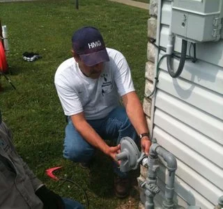 Technician kneeling to inspect a utility connection at the base of a building.