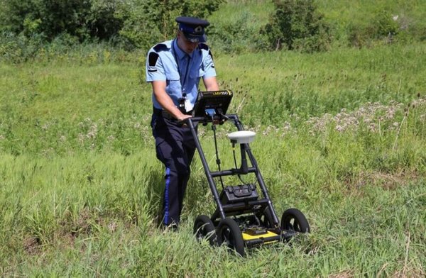 Law enforcement officer using a Radiodetection LMX200 GPR cart to survey a grassy field for buried evidence.