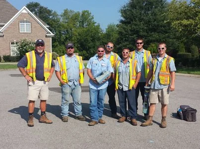 Group photo of a locate crew in high-visibility vests on a residential driveway.