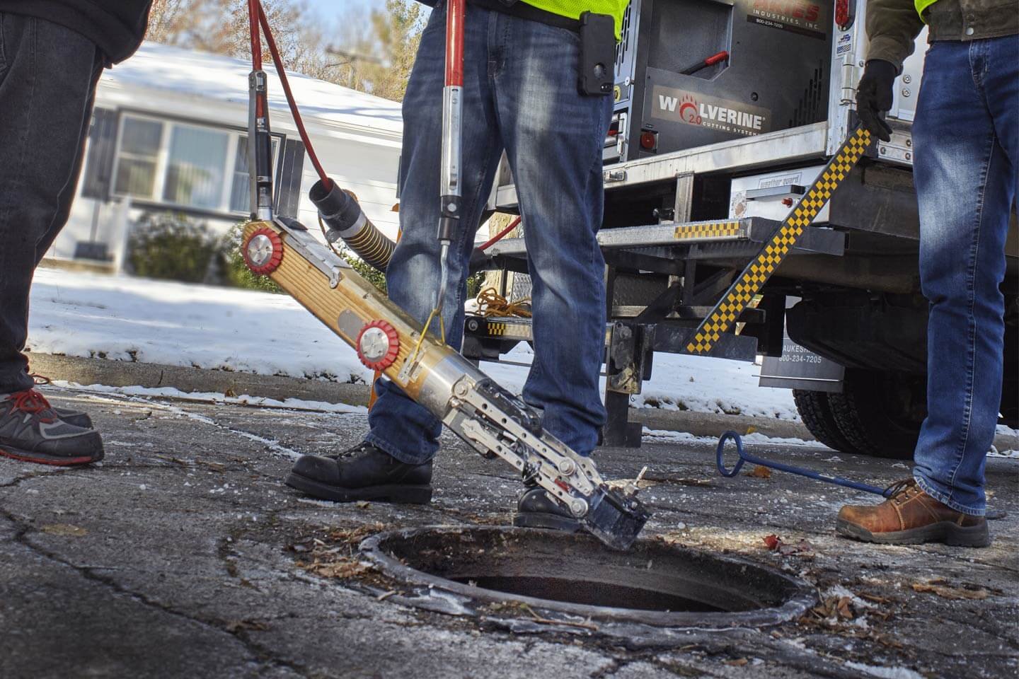 Technicians lowering the Aries Wolverine robotic cutting crawler into a manhole at a job site.