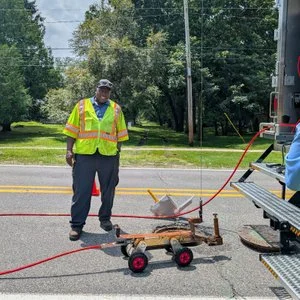 Technician standing on a paved road with a utility marking cart and traffic cones.