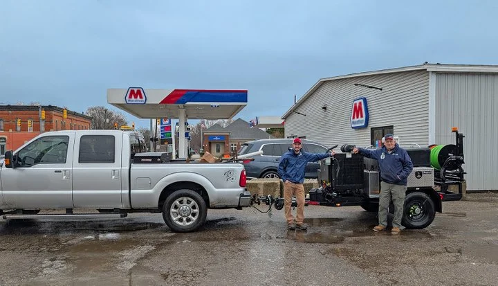 Technicians standing beside a truck and towed Harben hydro jetting trailer unit at a service delivery location.