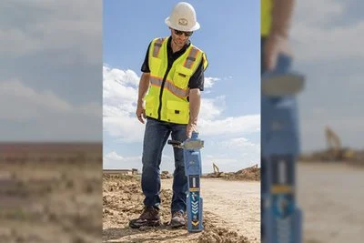 Technician in a safety vest operating a Radiodetection RD8200SG locator at an open desert construction site.